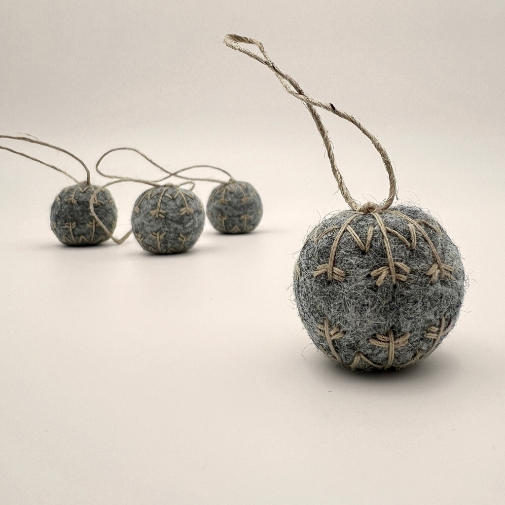 Four small felt snowflakes in Charcoal Marle with beige stitching.