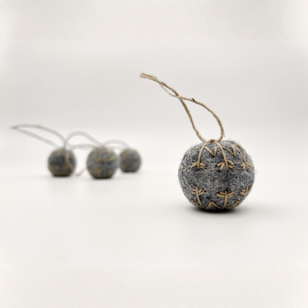 Four small felt snowflakes in Charcoal Marle with beige stitching.