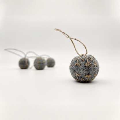 Four small felt snowflakes in Charcoal Marle with beige stitching.