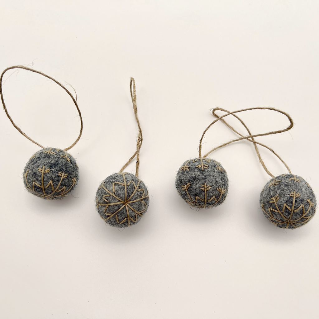 Four small felt snowflakes in Charcoal Marle with beige stitching.