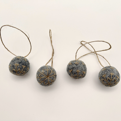 Four small felt snowflakes in Charcoal Marle with beige stitching.