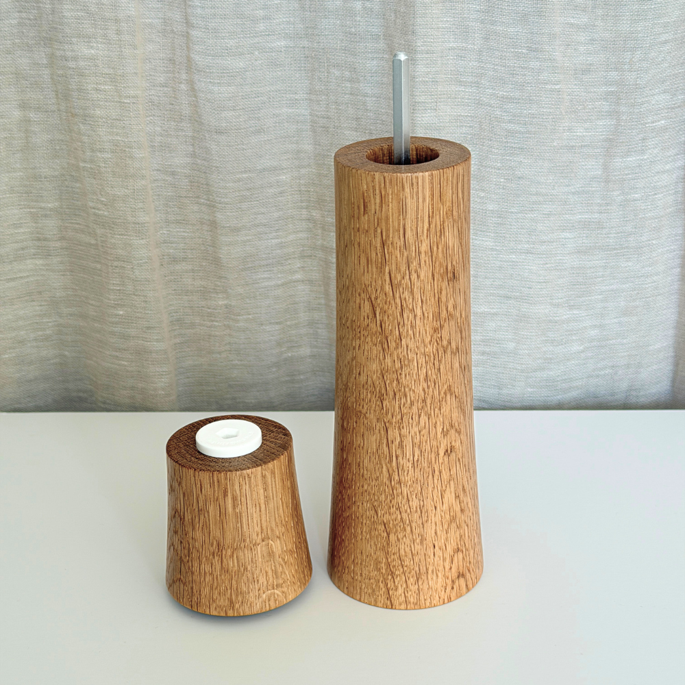 Large Pebble Studio Salt & Pepper Mill in American Oak with the top sitting next to the base. Minimalist design on a neutral background