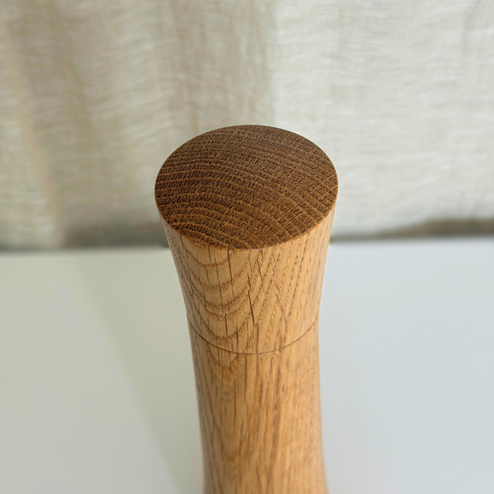 Curved top of a Pebble Studio Salt & Pepper Mill in American Oak. Minimalist design on a neutral background