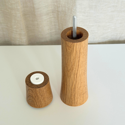 A Pebble Studio Salt & Pepper Mill in American Oak with the top placed next to the base. Minimalist design on a neutral background