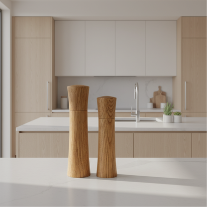 Two American Oak salt and pepper mills, standing side-by-side on a white kitchen countertop in a modern kitchen setting.