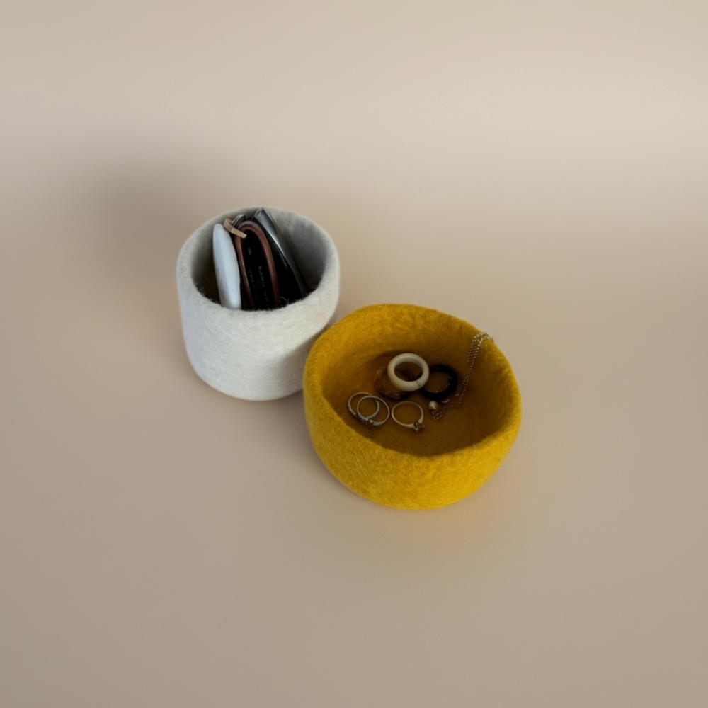Two small wool bowls, one white and one yellow, containing jewellery on a beige background