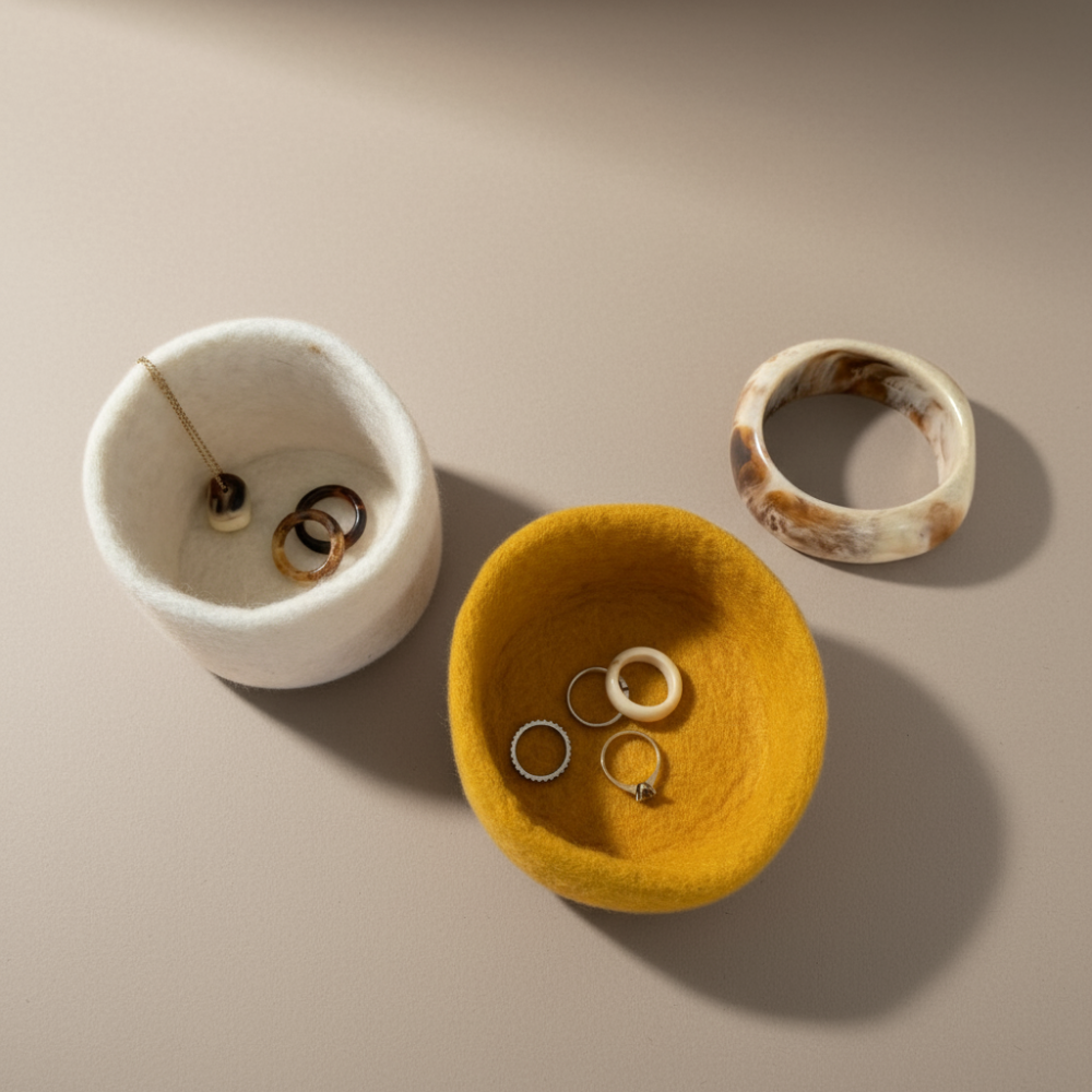 Two wool  jewellery bowls, one white and one yellow, with rings on a beige background.