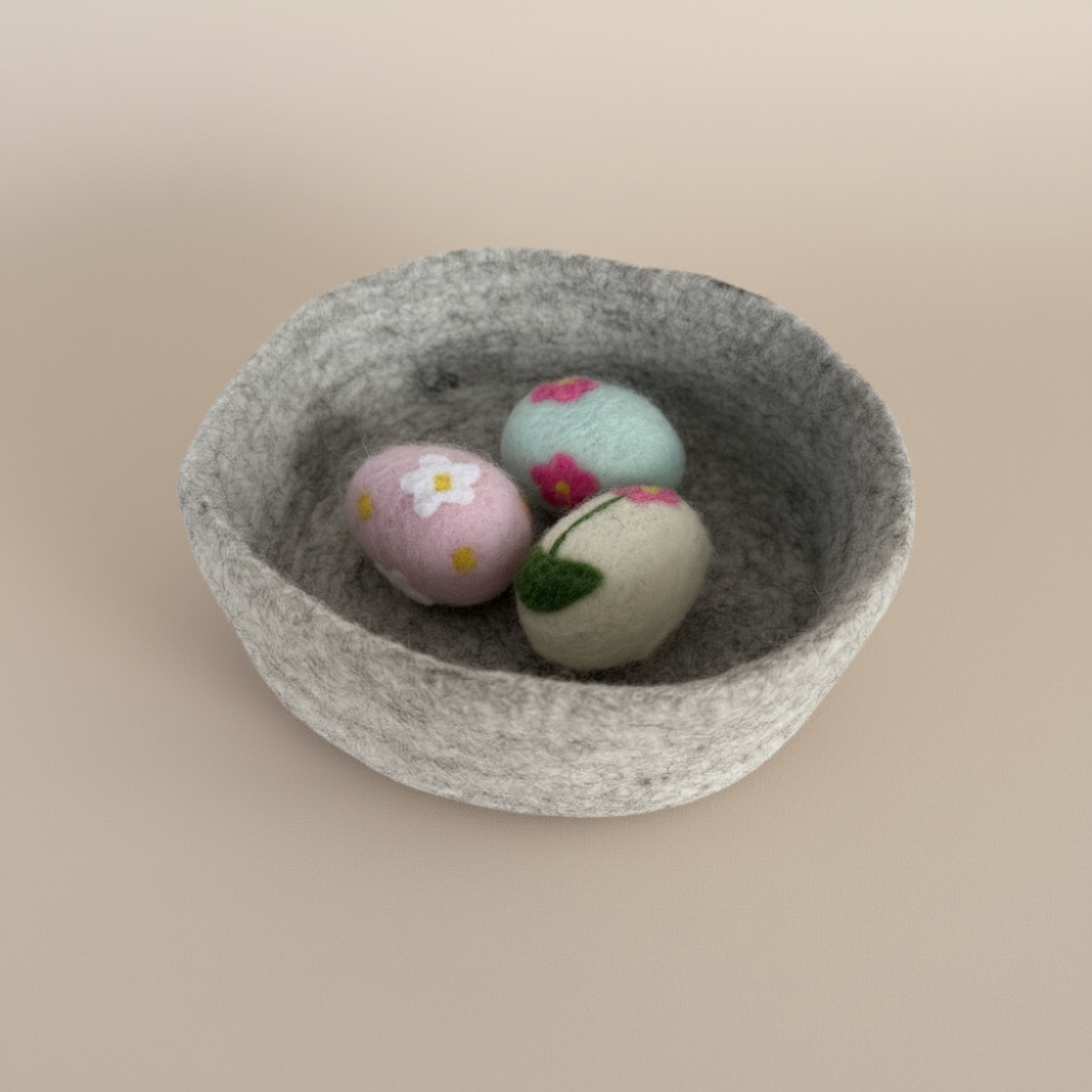 Grey felt bowl with three colourful felted balls on a beige background