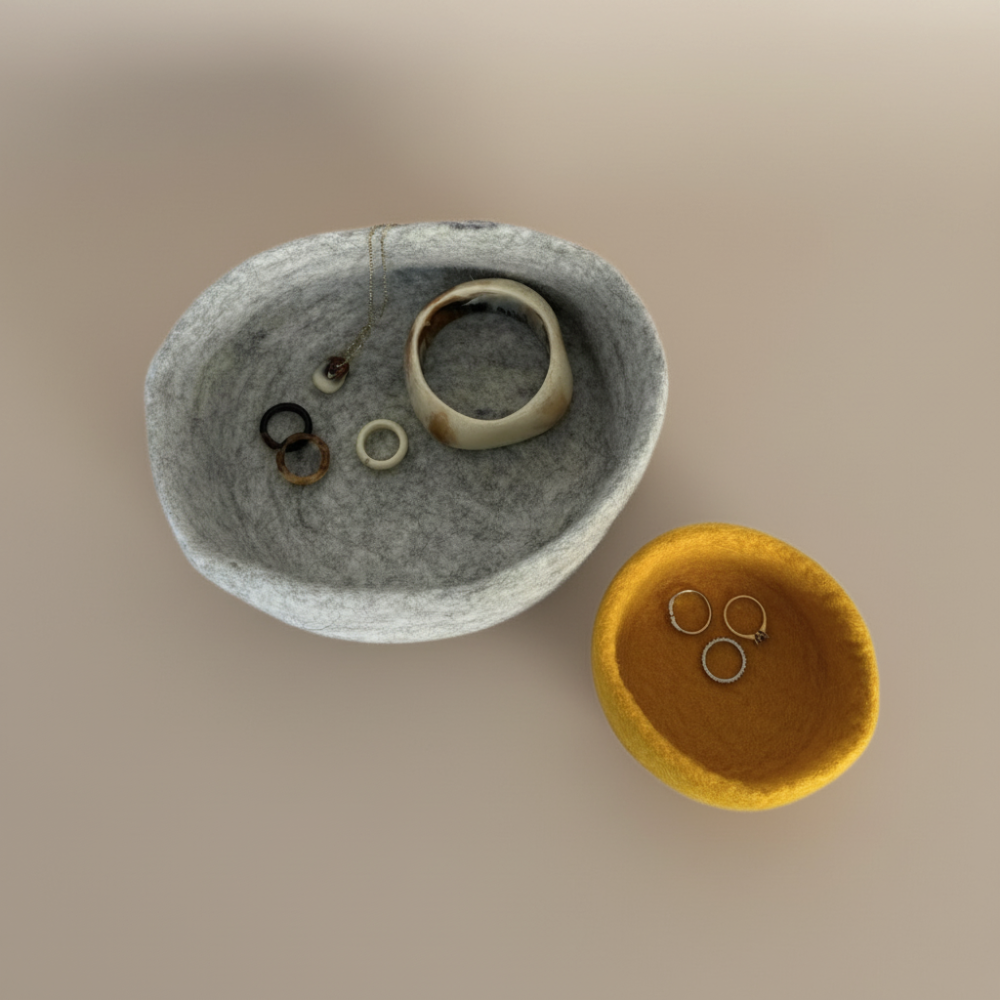 Handmade wool felt nesting bowls holding jewellery- one medium bowl in marbled beige and one small bowl in sunflower yellow, displayed on light background