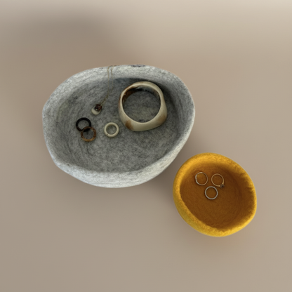 Handmade wool felt nesting bowls holding jewellery- one medium bowl in marbled beige and one small bowl in sunflower yellow, displayed on light background