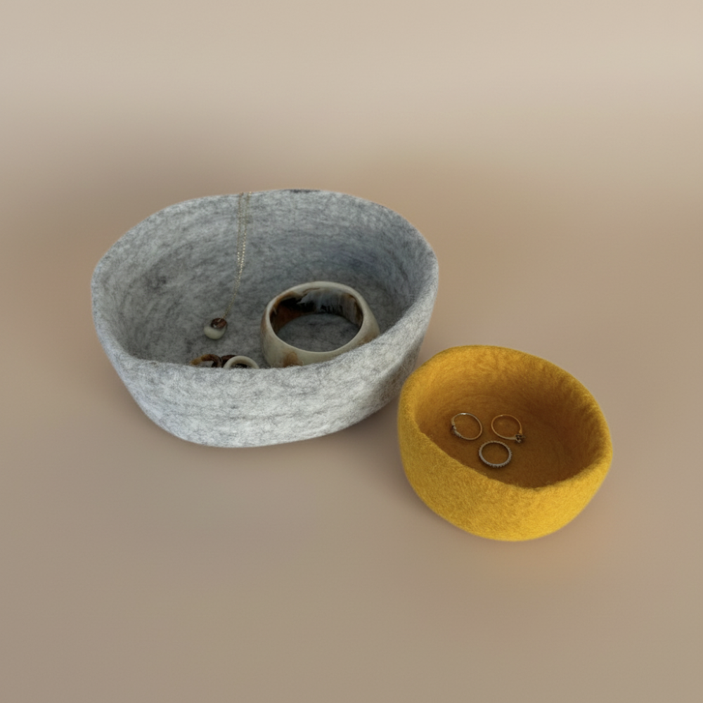 Two felted bowls holding jewellery, one grey and one yellow, on a beige background.