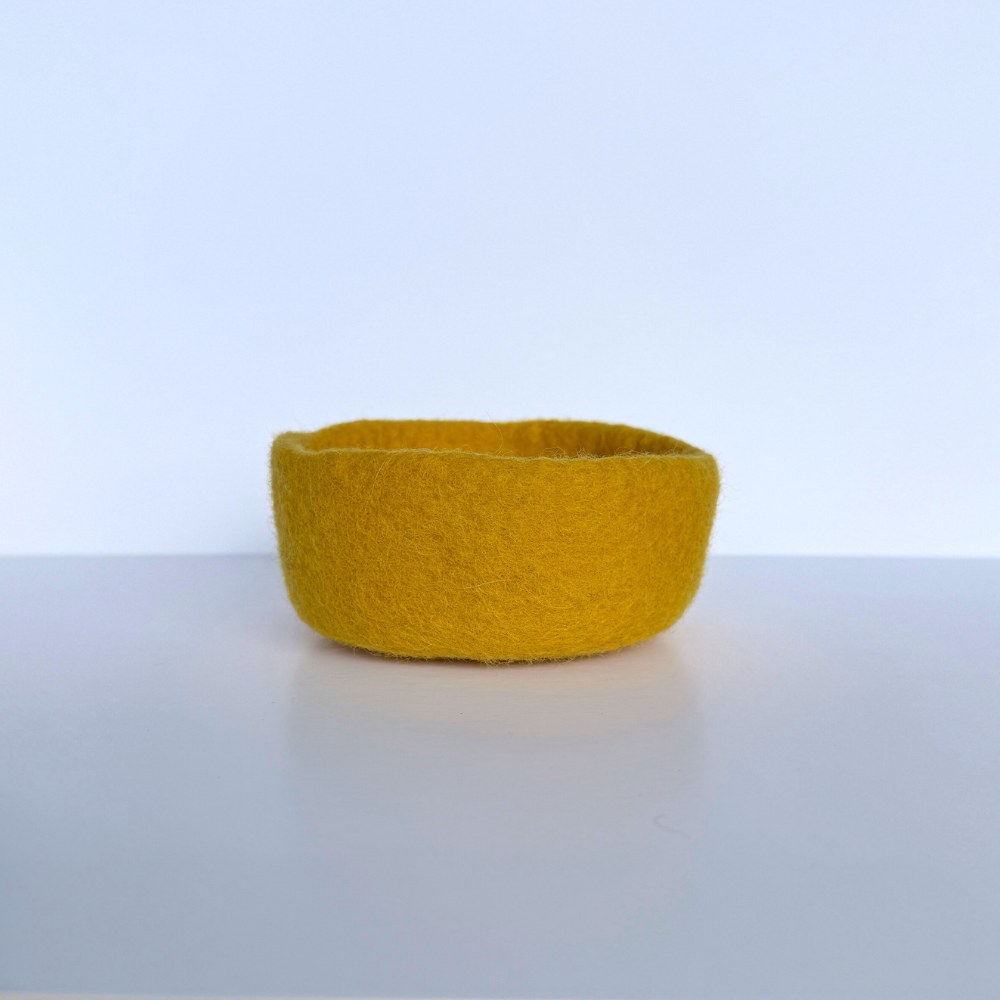 Yellow felted bowl on a light gray surface with a white background