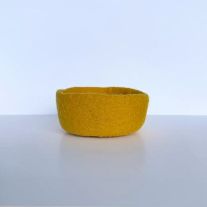 Yellow felted bowl on a light gray surface with a white background