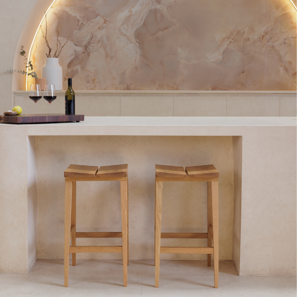 Two wooden bar stools in front of a stone wall with a decorative archway.