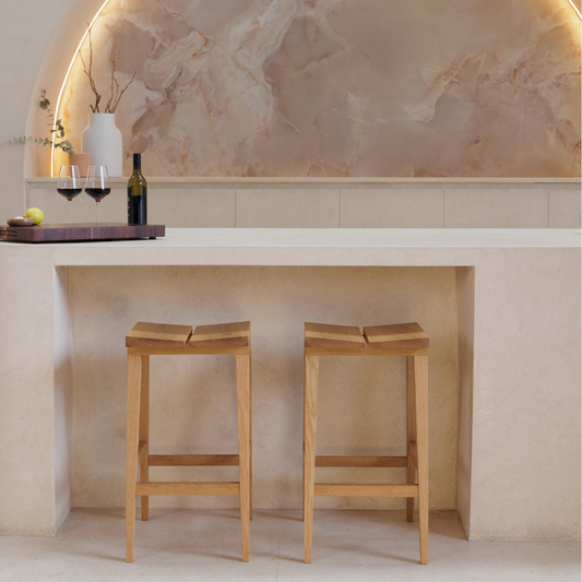 Two wooden bar stools in front of a stone wall with a decorative archway.