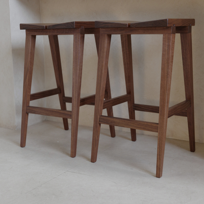 Two wooden bar stools against a plain wall.