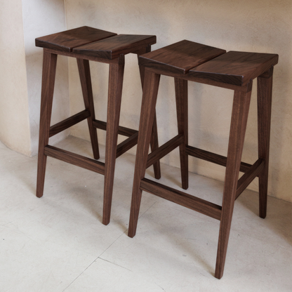 Two wooden bar stools on a light-colored floor with a neutral wall background.