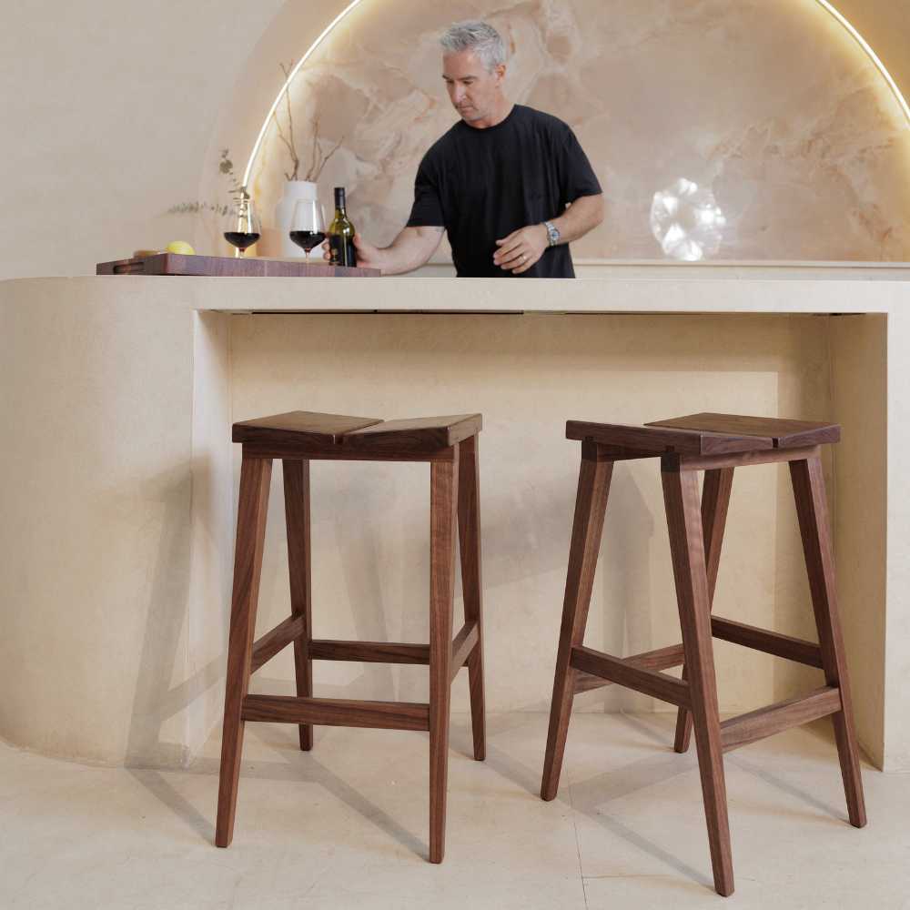 Two wooden bar stools in front of a counter with a person behind it.