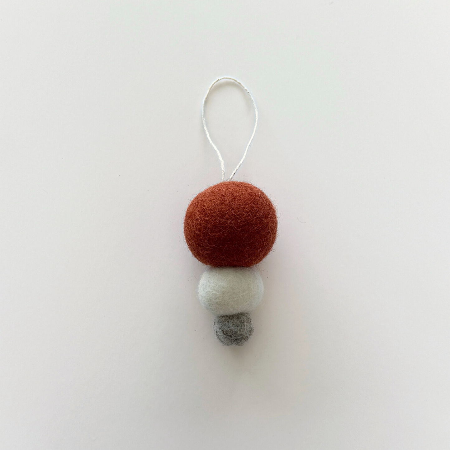 Pebble Studio Nordic Bauble in rust: three stacked felt spheres made from New Zealand wool with a hanging loop.