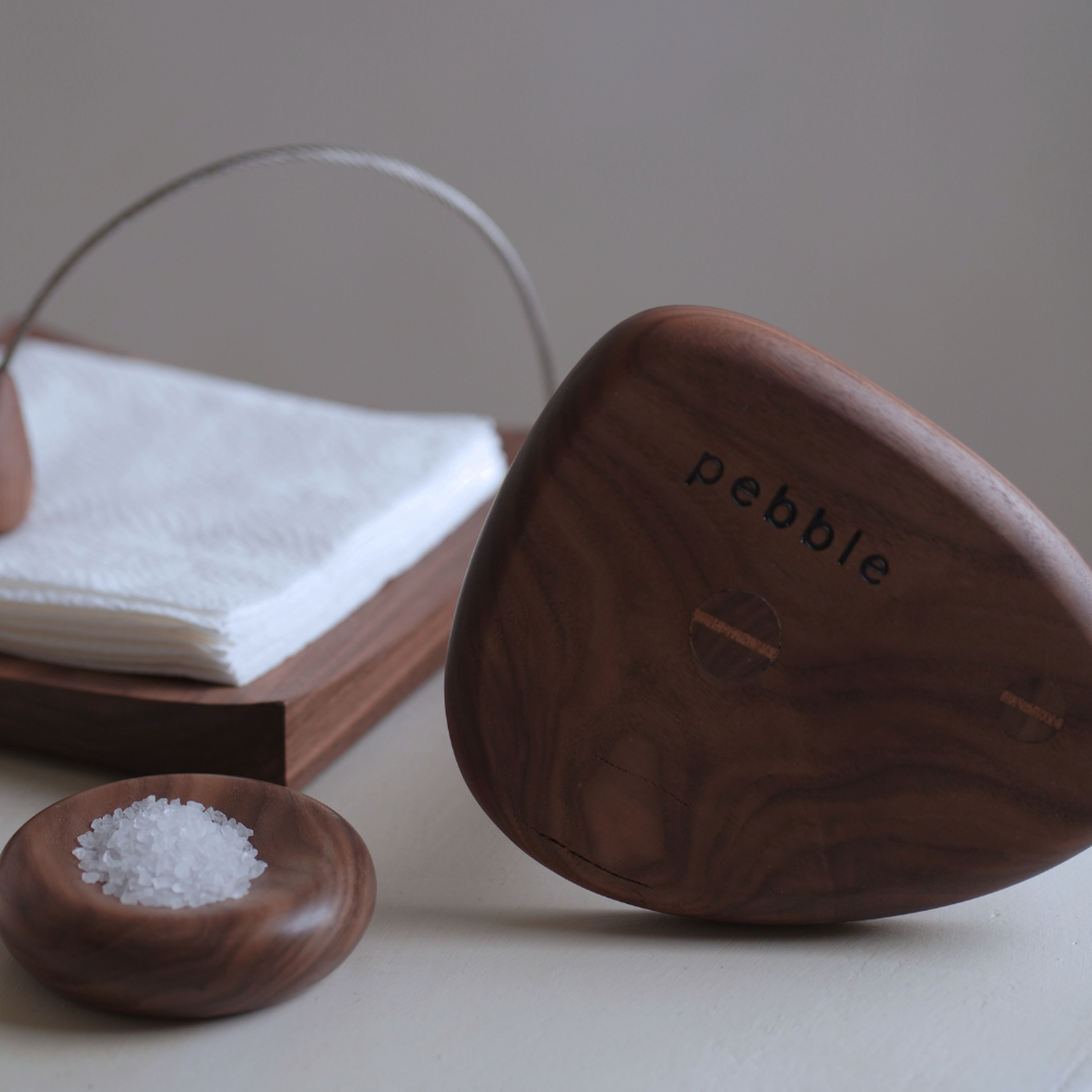 Base of wooden paper towel holder with 'pebble' branding next to a small wooden salt dish on a neutral background.