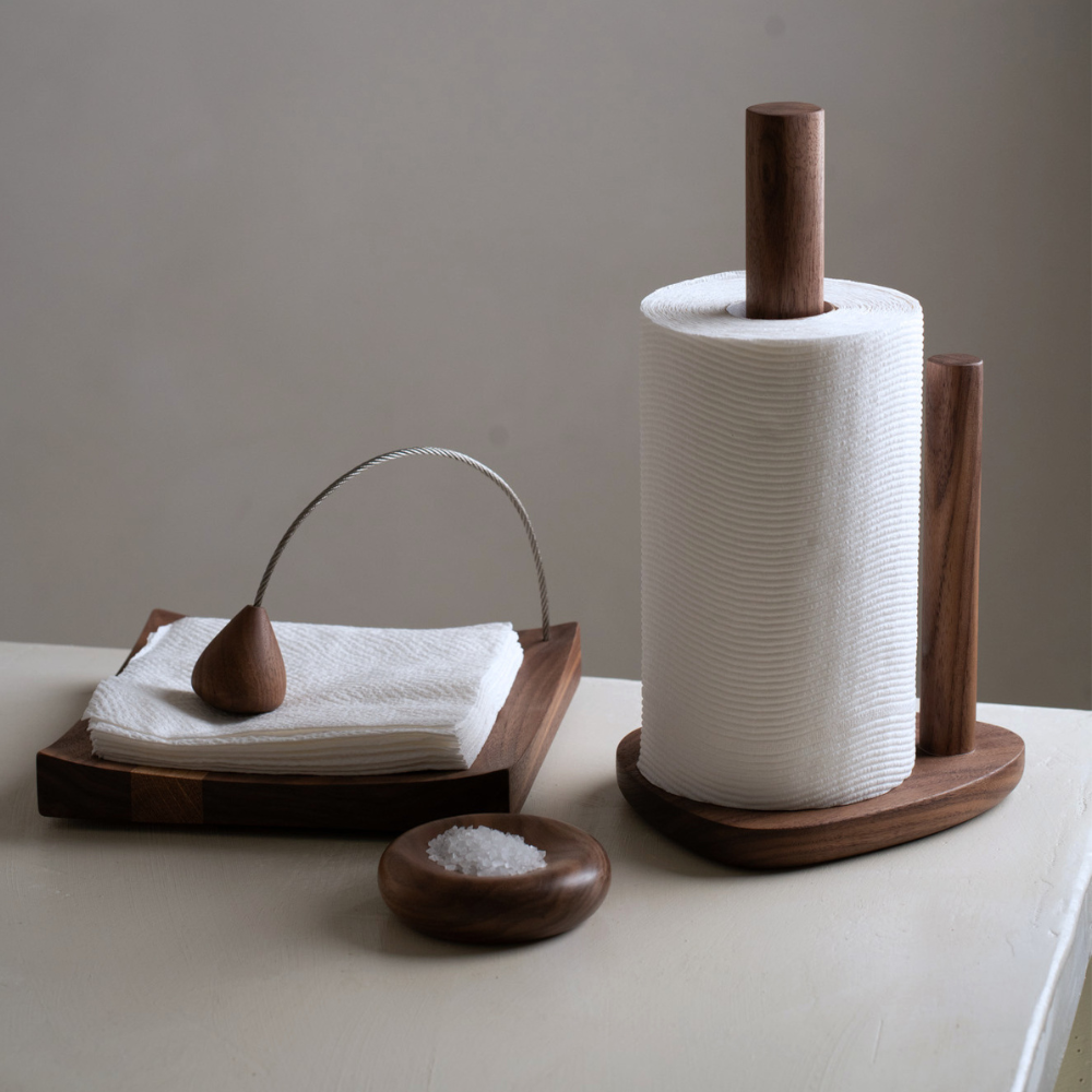 Wooden paper towel holder with a roll of paper towels, wooden napkin holder with napkins, and small wooden salt dish on a neutral background.