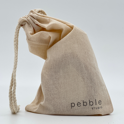 Calico drawstring bag with 'pebble studio' branding on a light grey background