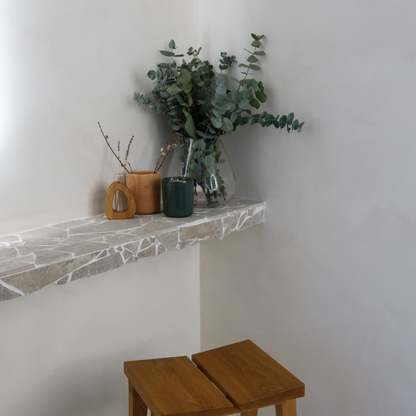Decorative shelf with plants and a wooden stool against a white wall.
