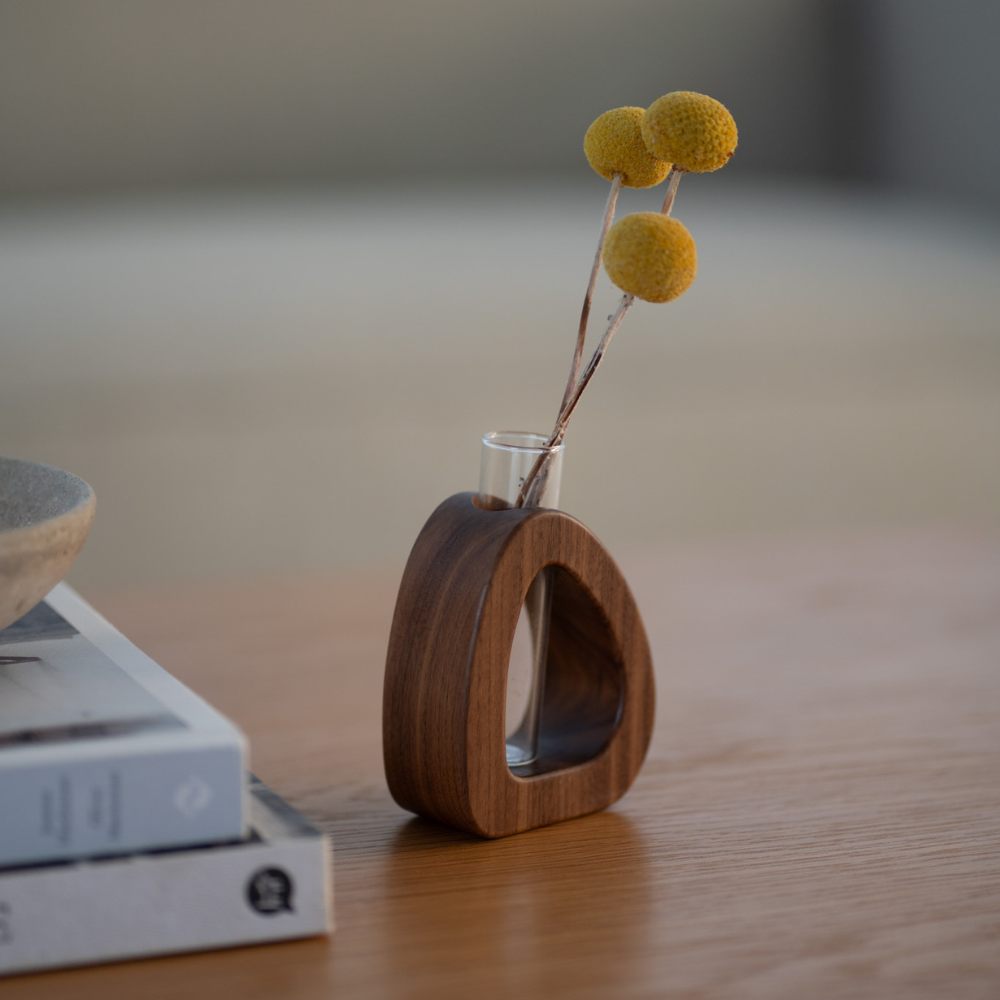 Wooden vase with a clear glass insert holding yellow flowers on a wooden surface.