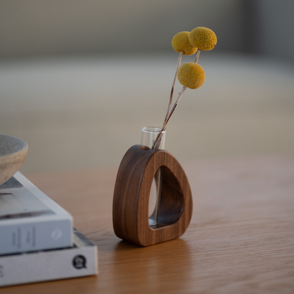 Wooden vase with a clear glass insert holding yellow flowers on a wooden surface.