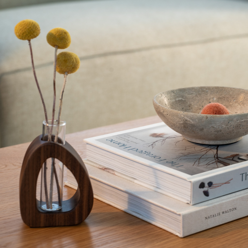 Wooden vase with dried plants next to a stack of books and stone bowl.