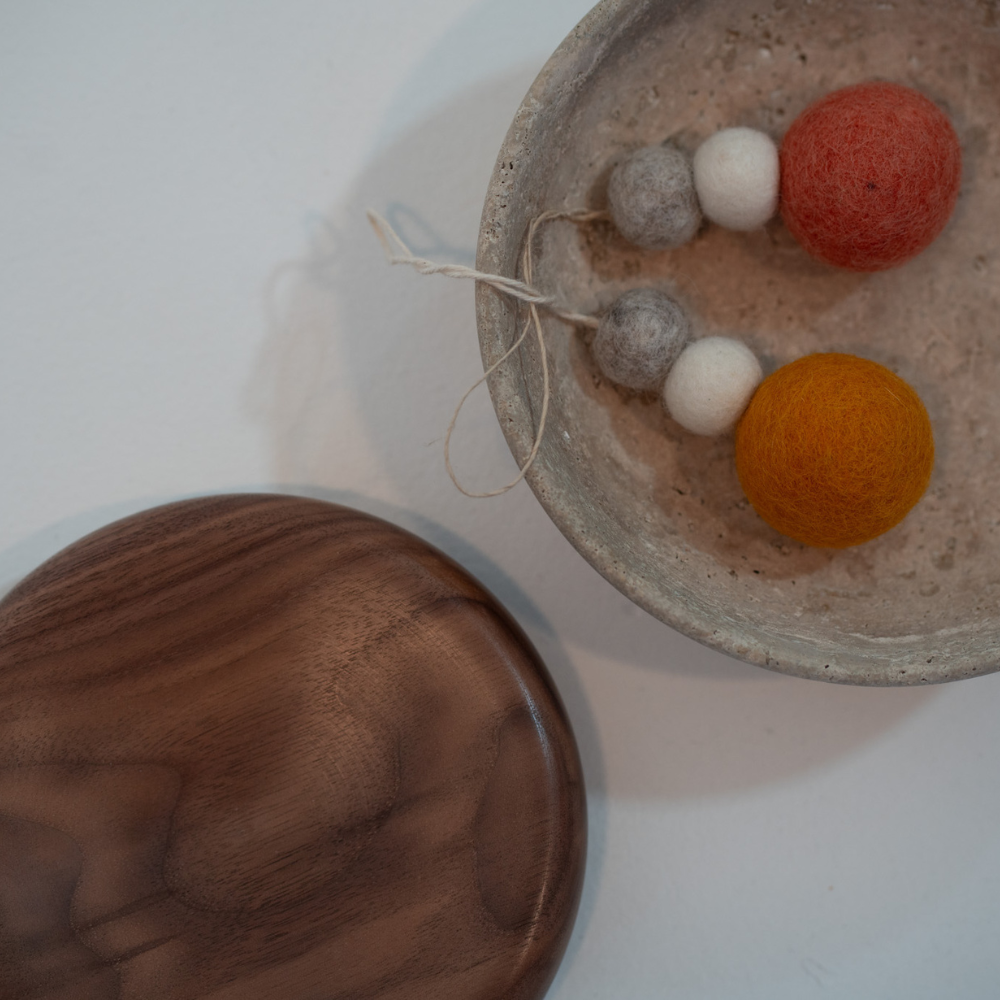 Hand-felted wool hanging diffusers sitting in a stone dish, styled next to a wood dish by Pebble Studio