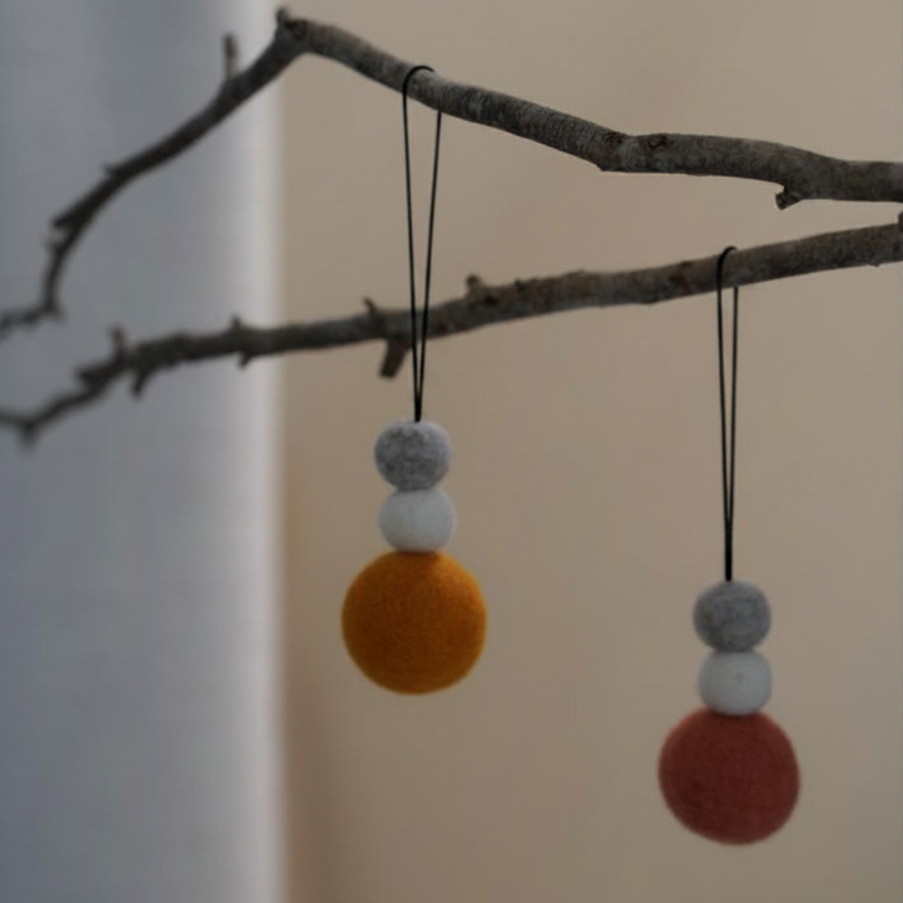 Felt ball hanging decorations, hanging from a branch against a neutral background