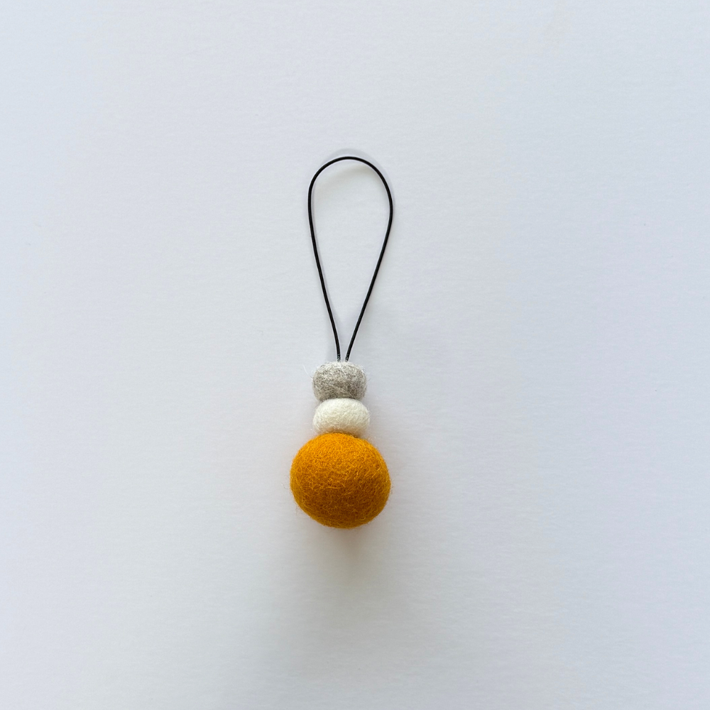 Bright saffron yellow wool hanging diffuser with natural and grey felt accent beads, handcrafted and displayed on white backdrop. Designed for use with essential oils.