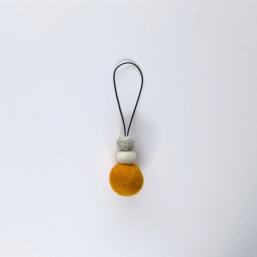 Bright saffron yellow wool hanging diffuser with natural and grey felt accent beads, handcrafted and displayed on white backdrop. Designed for use with essential oils.