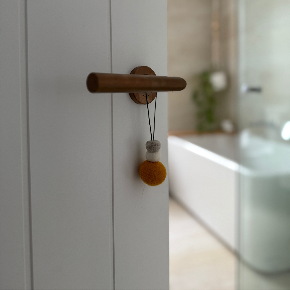 Bright saffron yellow wool hanging diffuser with natural and grey felt accent beads, hanging from a door handle. Designed for use with essential oils.