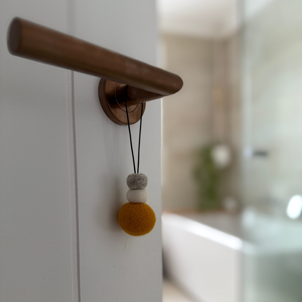 Bright saffron yellow wool hanging diffuser with natural and grey felt accent beads, hanging from a door handle. Designed for use with essential oils.