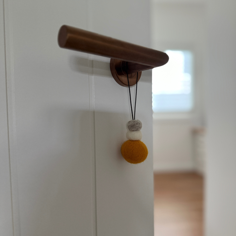 Bright saffron yellow wool hanging diffuser with natural and grey felt accent beads, hanging from a door handle. Designed for use with essential oils.