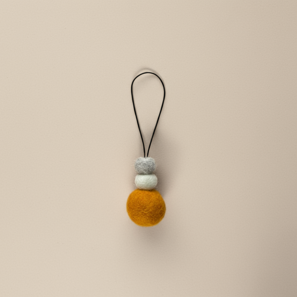 Bright saffron yellow wool hanging diffuser with natural and grey felt accent beads, handcrafted and displayed on a light backdrop. Designed for use with essential oils.