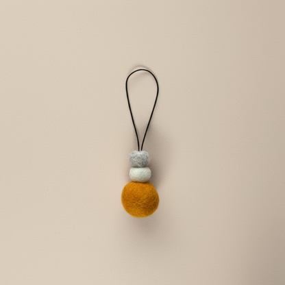 Bright saffron yellow wool hanging diffuser with natural and grey felt accent beads, handcrafted and displayed on a light backdrop. Designed for use with essential oils.
