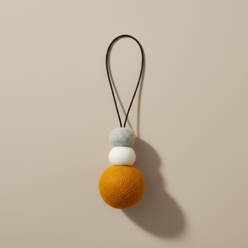 Bright saffron yellow wool hanging diffuser with natural and grey felt accent beads, handcrafted and displayed on light backdrop. Designed for use with essential oils.