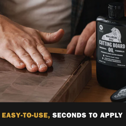 Person applying cutting board oil to a wooden cutting board with a bottle of Walrus Oil in the background.