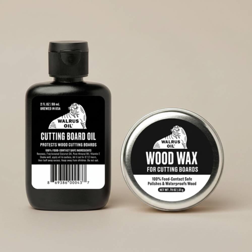 A black bottle of Walrus Oil Cutting Board Oil stands next to a round silver tin of Walrus Oil Wood Wax, both featuring black and white labels, on a solid beige background.