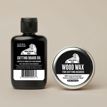 A black bottle of Walrus Oil Cutting Board Oil stands next to a round silver tin of Walrus Oil Wood Wax, both featuring black and white labels, on a solid beige background.