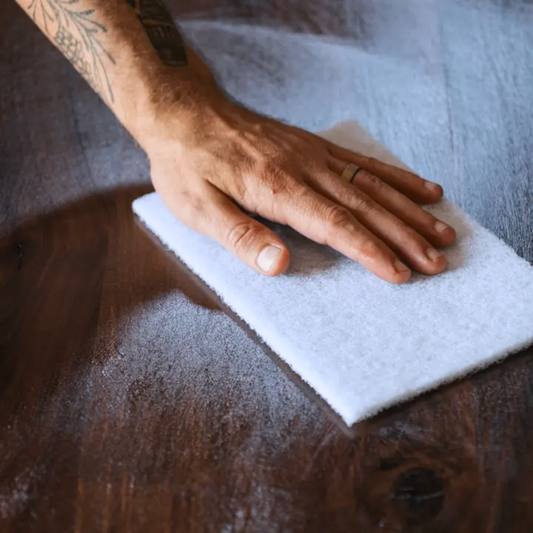 Hand holding a white polishing pad on a wooden surface