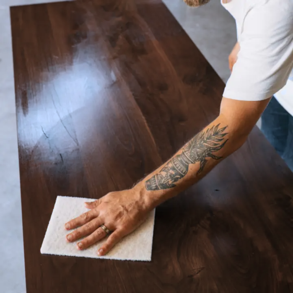 Person cleaning a wooden table with a Walrus Oil white polishing pad