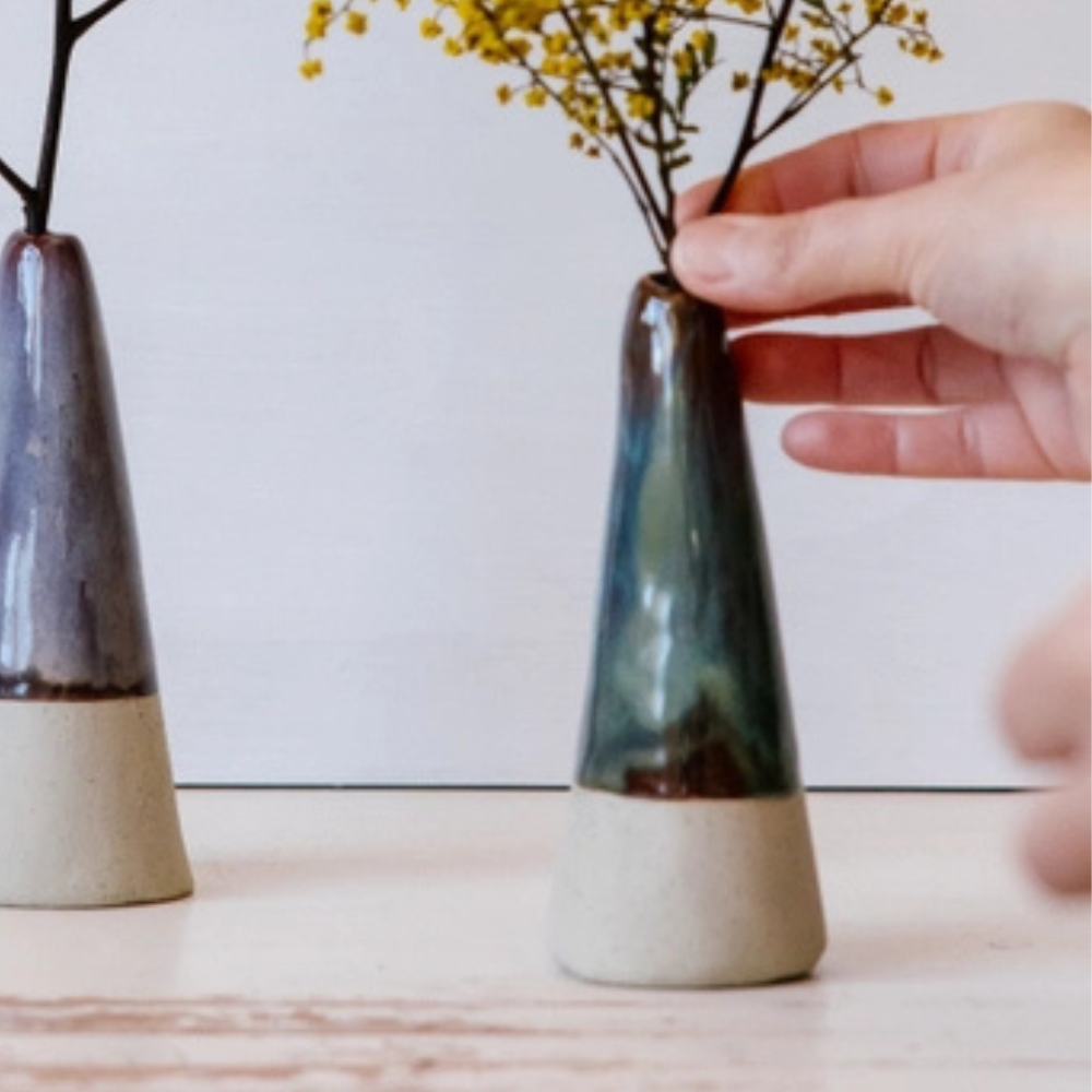 Person arranging flowers in a small ceramic vase on a wooden surface.