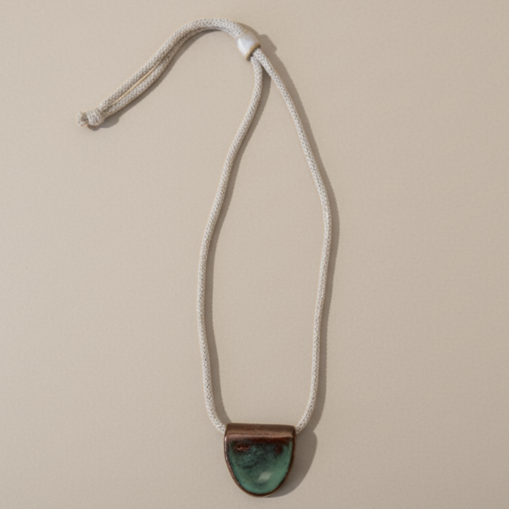 Necklace with a green ceramic pendant on a beige background