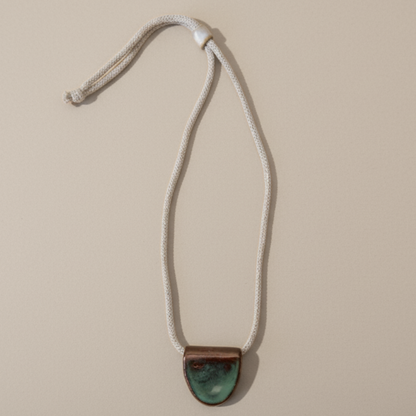 Necklace with a green ceramic pendant on a beige background