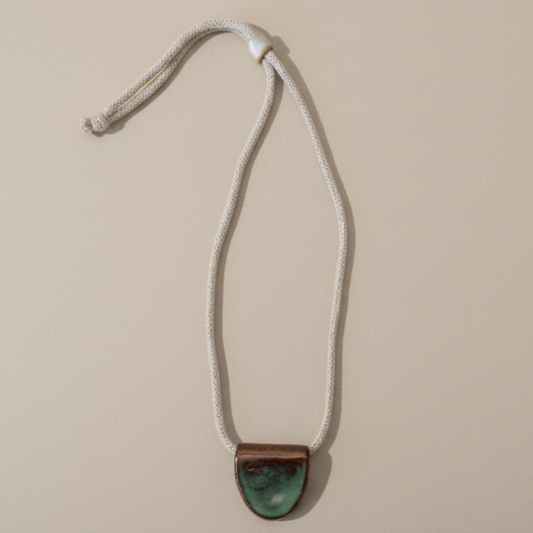 Necklace with a green ceramic pendant on a beige background