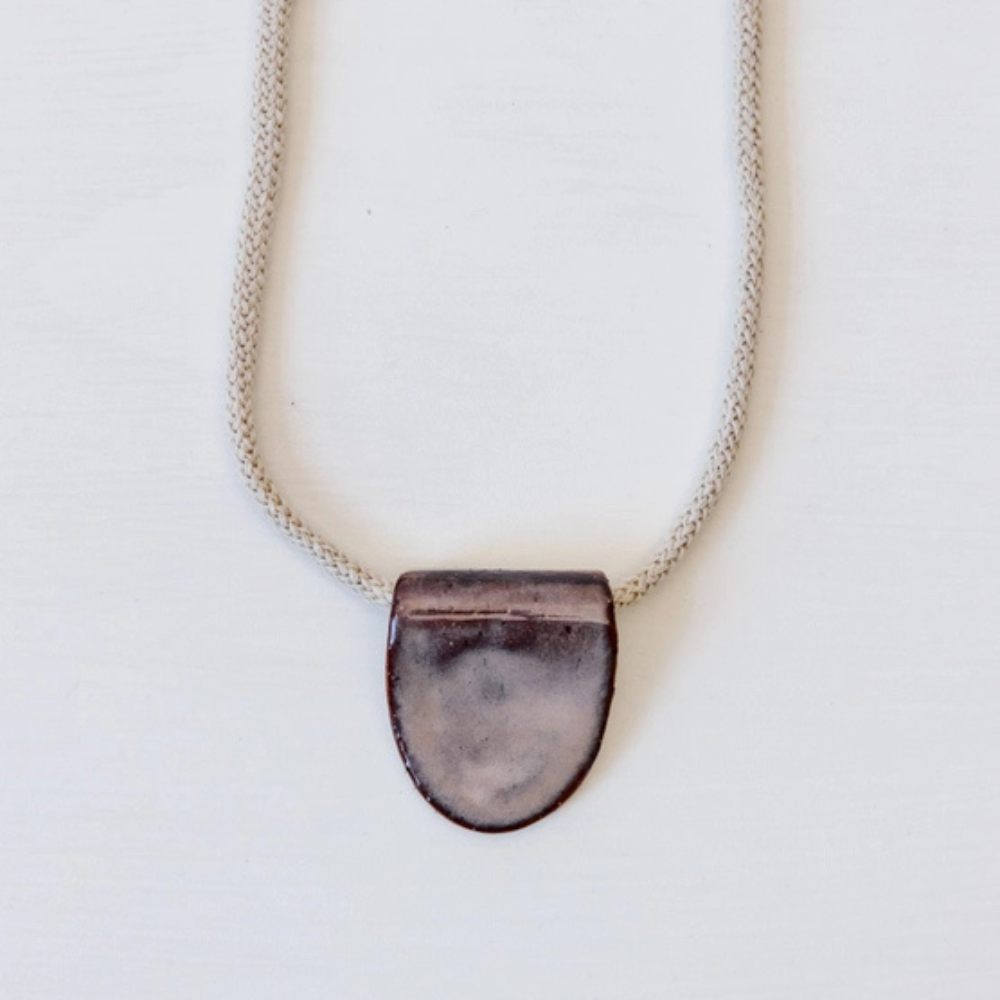 Necklace with a dark ceramic pendant on a light grey background
